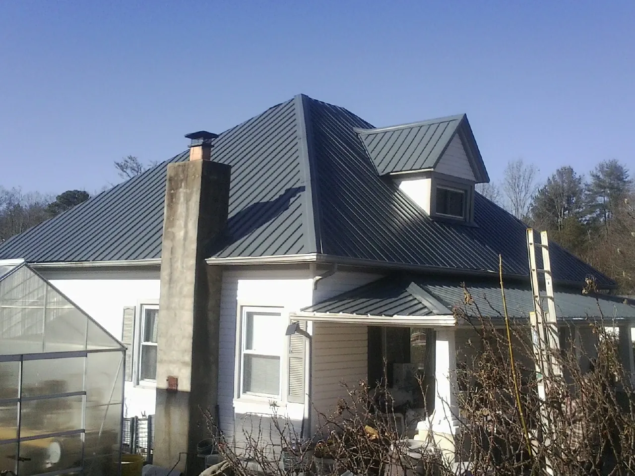 Dark blue standing seam metal roof on a white farmhouse with dormer — Slate & Tile Roof Repair by Roofing Brothers in Traverse City