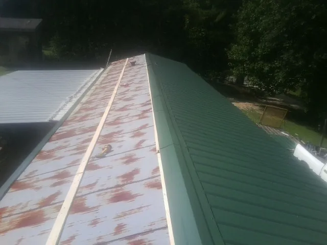 Old rusted panels beside newly installed green metal roofing — Wind Damage Roof Repair by Roofing Brothers in Traverse City