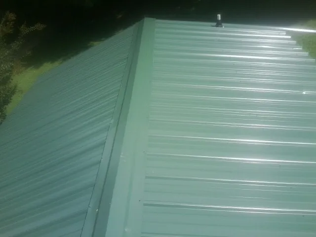 New green metal panels meeting at the ridge of a roof — Flat Roof Repair work by our crew in Traverse City
