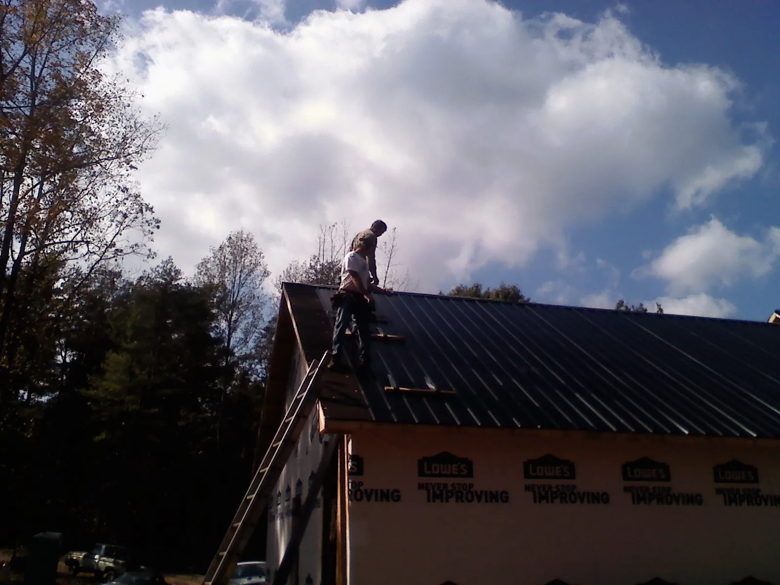 Roofer fastening dark metal panels high against a cloudy sky, from a Roof Inspection job in Traverse City
