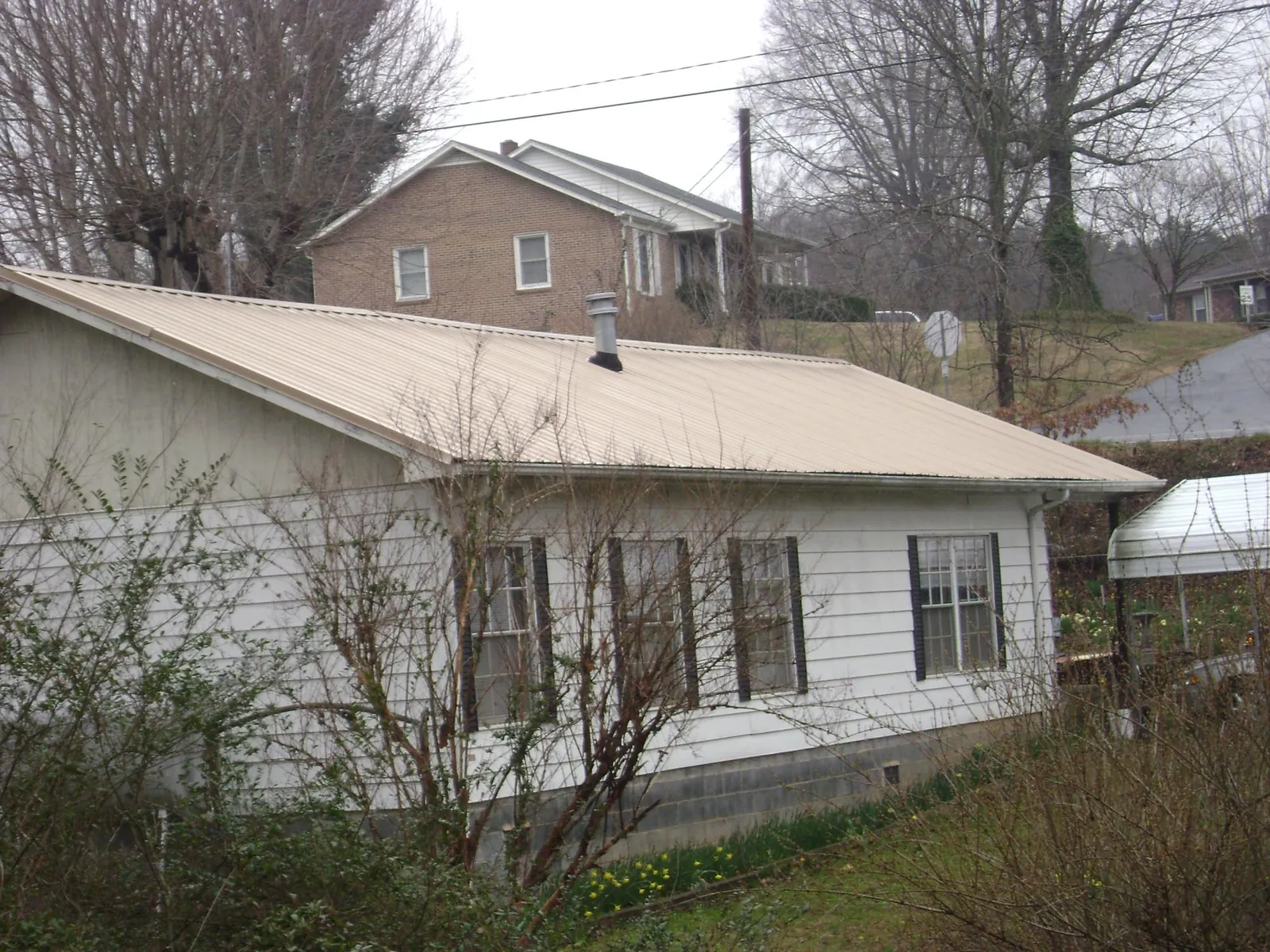 Tan metal roof on a white sided house set into a hillside — Commercial Roofing by Roofing Brothers in Traverse City