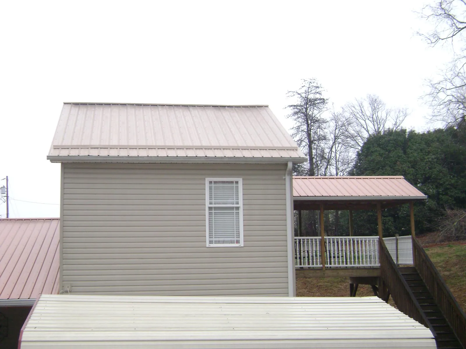 Tan metal roofs on a two story addition and attached porch, from a Roof Replacement job in Traverse City
