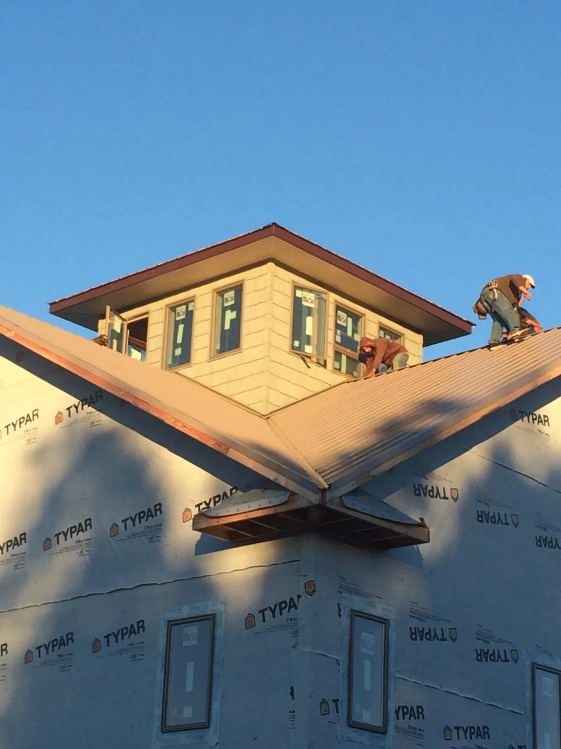 Roofers working around a rooftop cupola on a new metal roof at sunset — Roof Waterproofing in Traverse City by Roofing Brothers